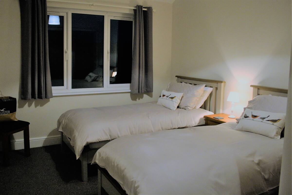 Una habitación de hotel con dos camas, una mesita de noche, una lámpara y una ventana con cortinas.