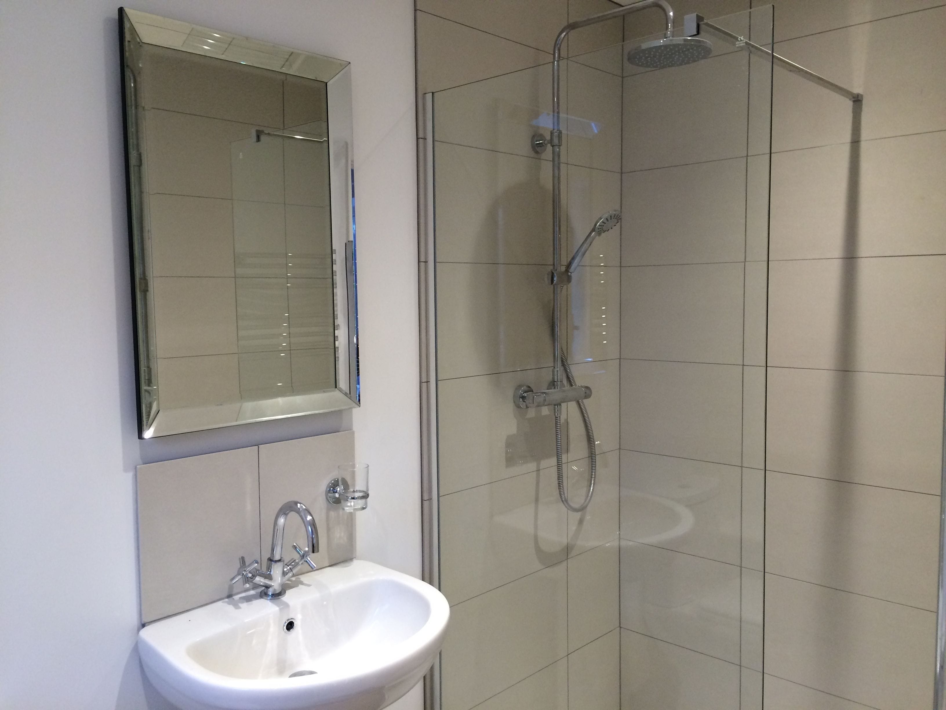 Een badkamer met een wit wastafel, een spiegel en een douche met glazen wanden.
