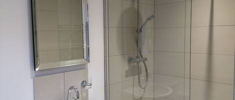 Een badkamer met een wit wastafel, een spiegel en een douche met glazen wanden.