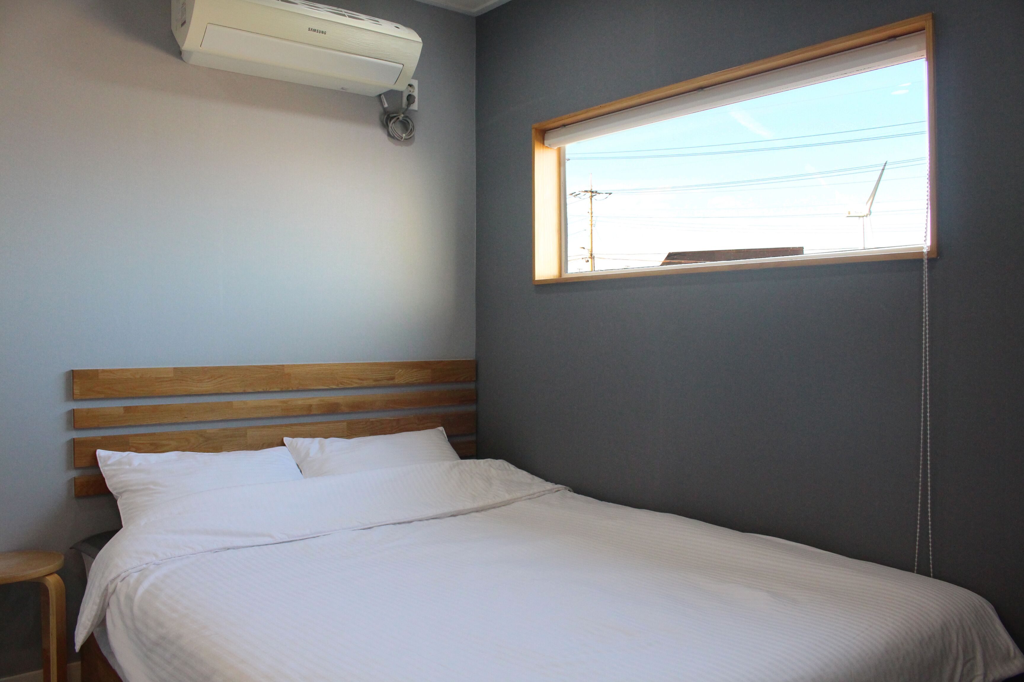 Een slaapkamer met een houten hoofdbord, een raam met zonwering en een airconditioner aan het plafond.