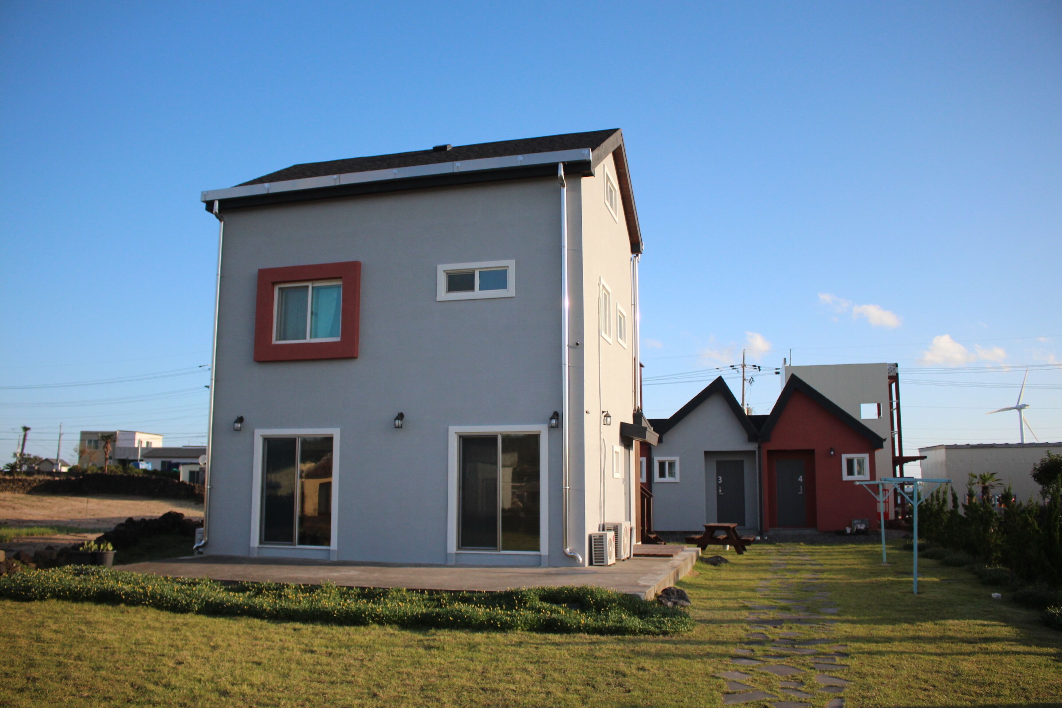 A modern two-story house with a red front door, a garage, and a small patio area.