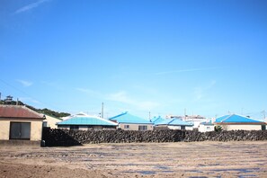 A residential area with houses having blue roofs, a stone wall, and a dirt ground. - September Pension (Jeju City)