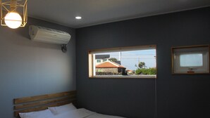 Quarto de hotel com cama, janela com vista para edifícios, ar condicionado e luminária fixada na parede.