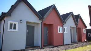 Uma fileira de casas modernas com números de porta distintos, um caminho de acesso de cascalho e um céu claro.