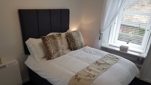 A bed with a dark headboard, white bedding, and decorative pillows. - Riverside Apartments (Carluke)