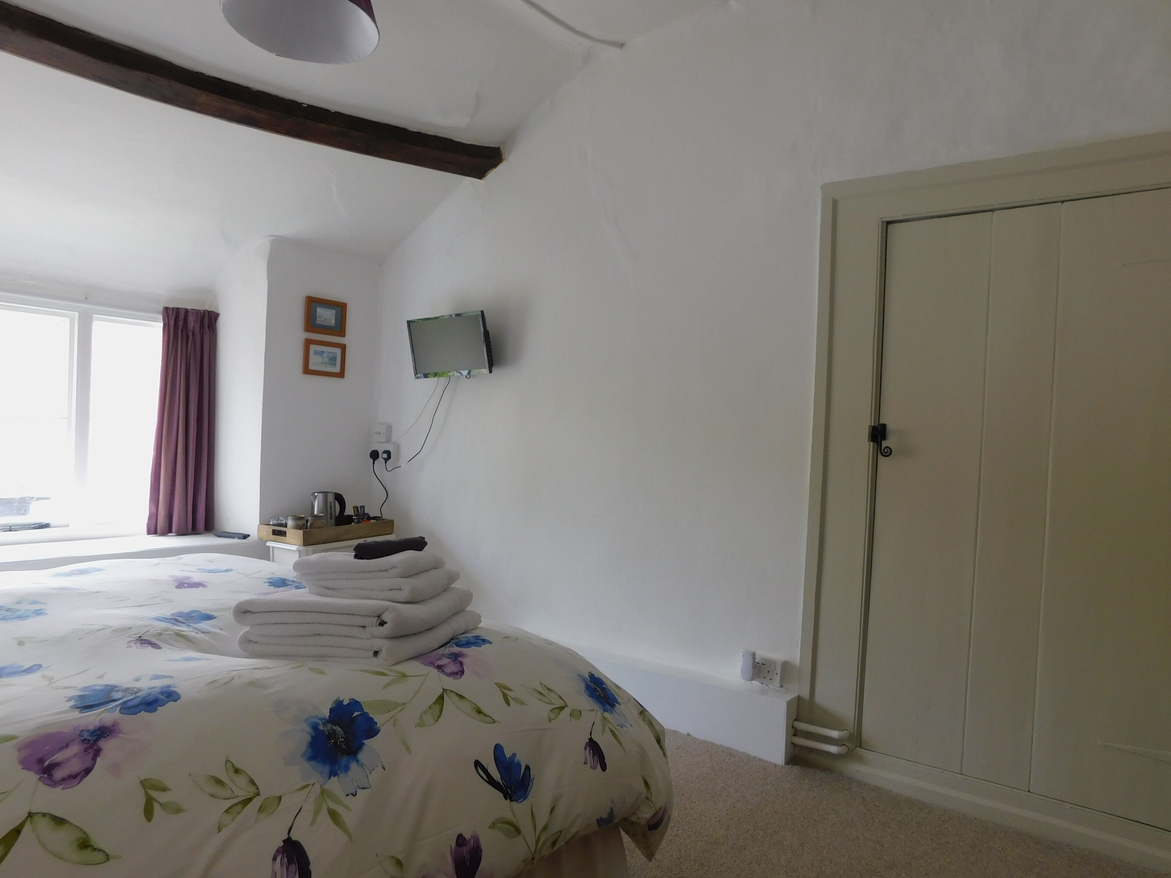 Un dormitorio con una cama grande, un televisor montado en la pared, una ventana con cortinas y una puerta.