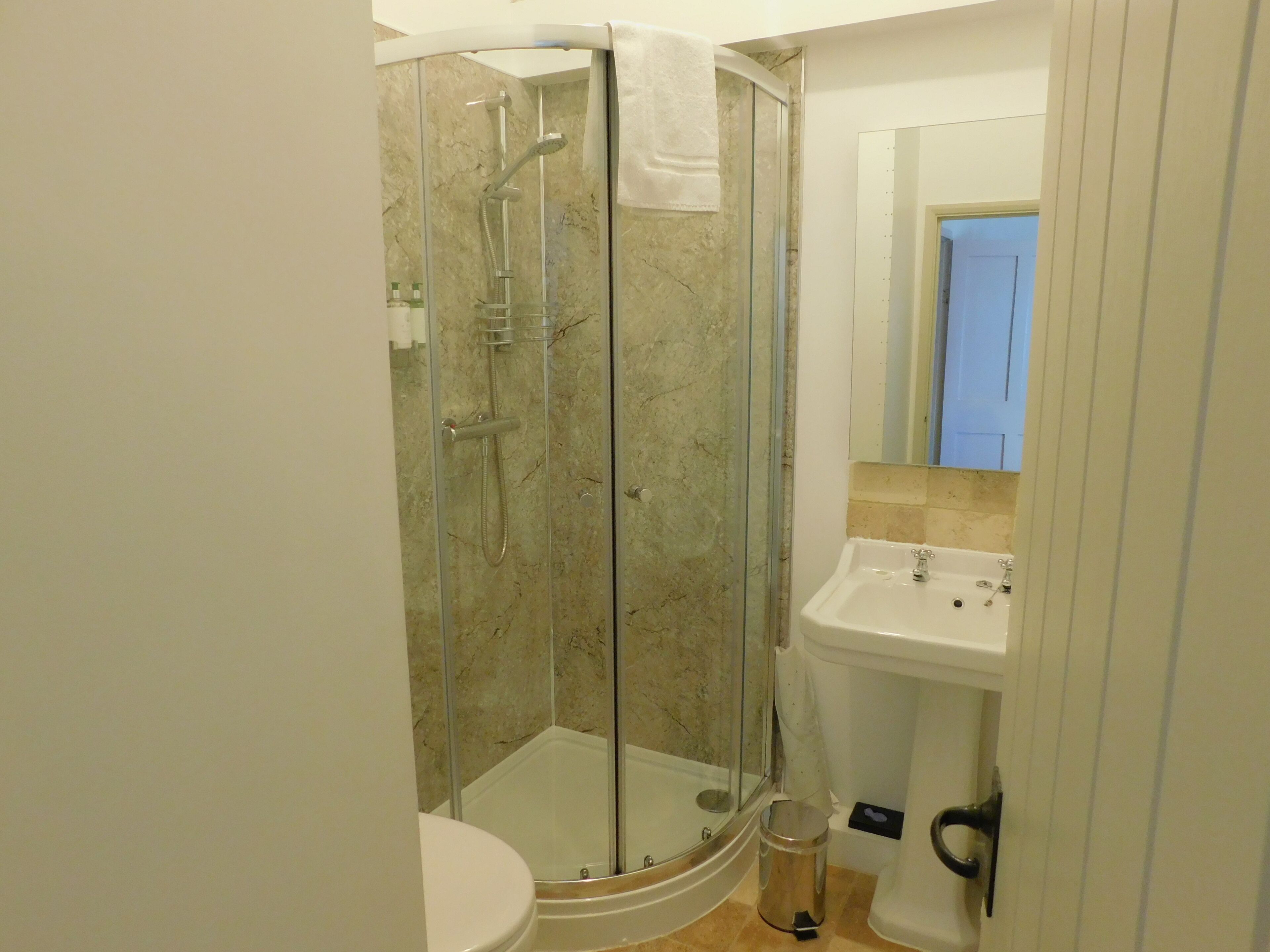 Un bany modern amb plat de dutxa tancat amb vidre, un vàter blanc i un lavabo amb mirall a la part superior.