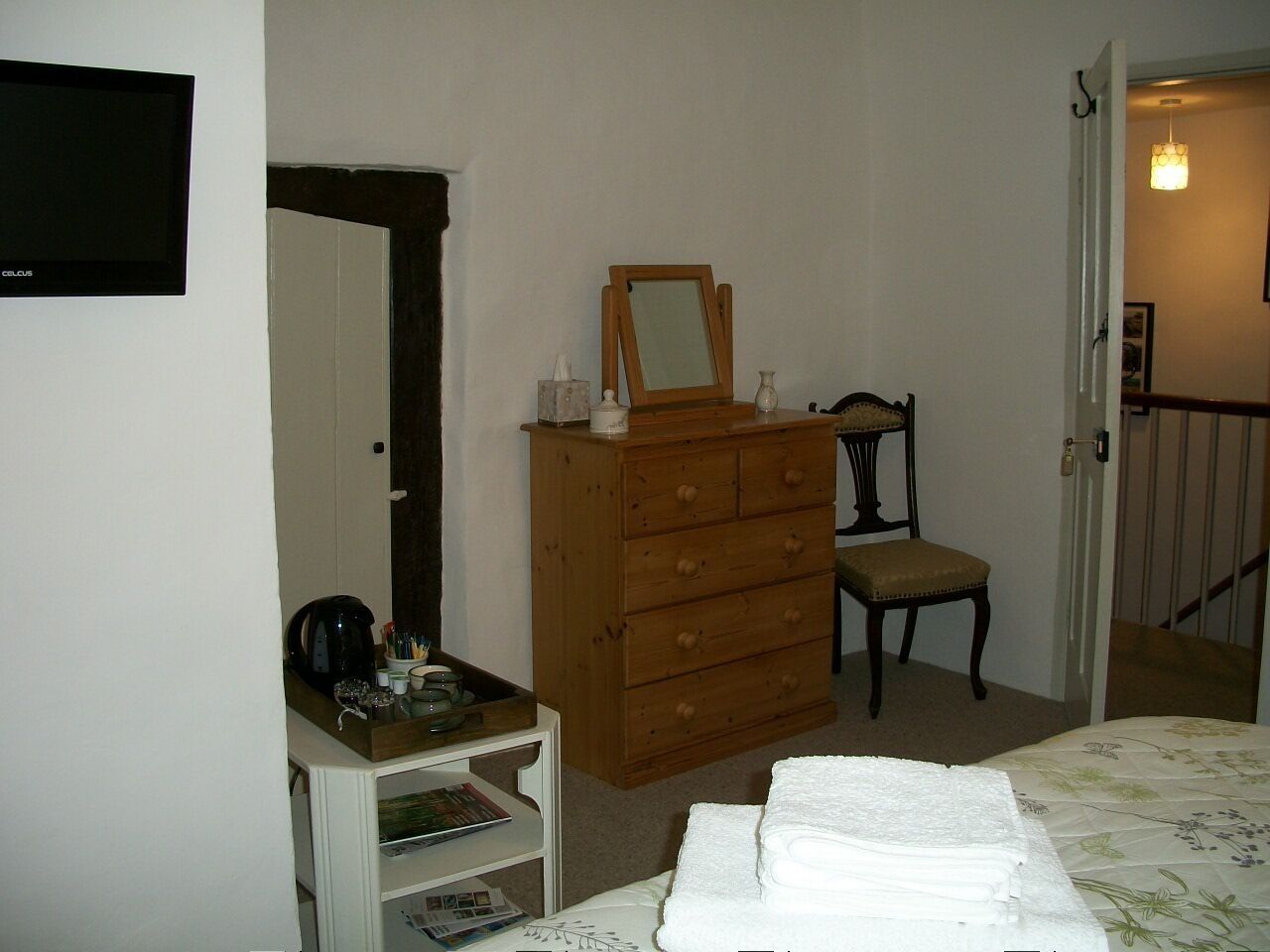 Un dormitorio con cómoda de madera, una silla, una cama con colcha floral y un televisor en la pared.