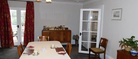 A dining room with a table set for four, a wooden cabinet, and a door leading to a balcony.