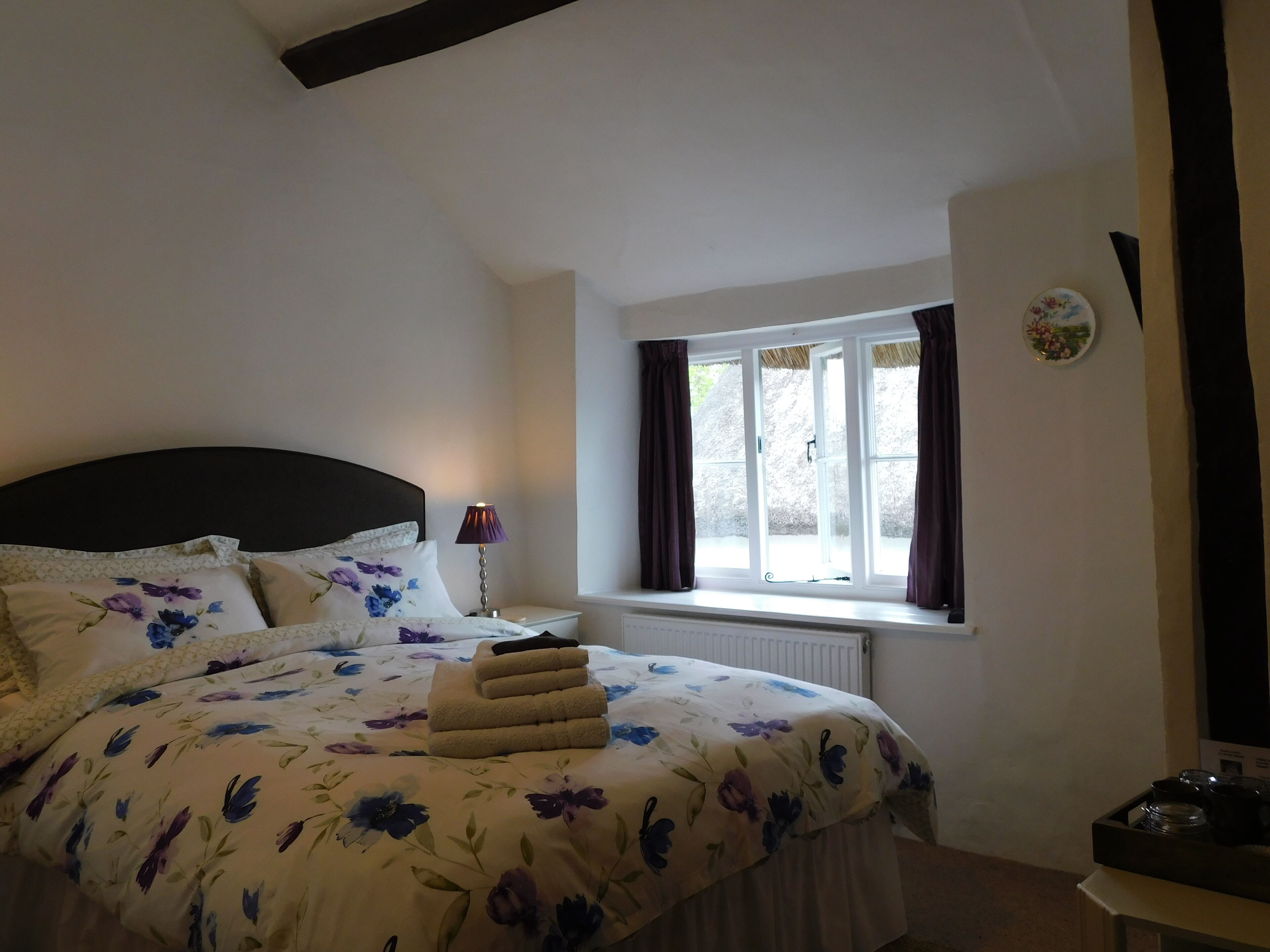 A bedroom with a bed, a nightstand, a lamp, a window with curtains, and a radiator.