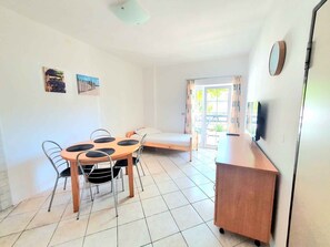 A room with a bed, a table with chairs, a small cabinet, and a television on the wall.