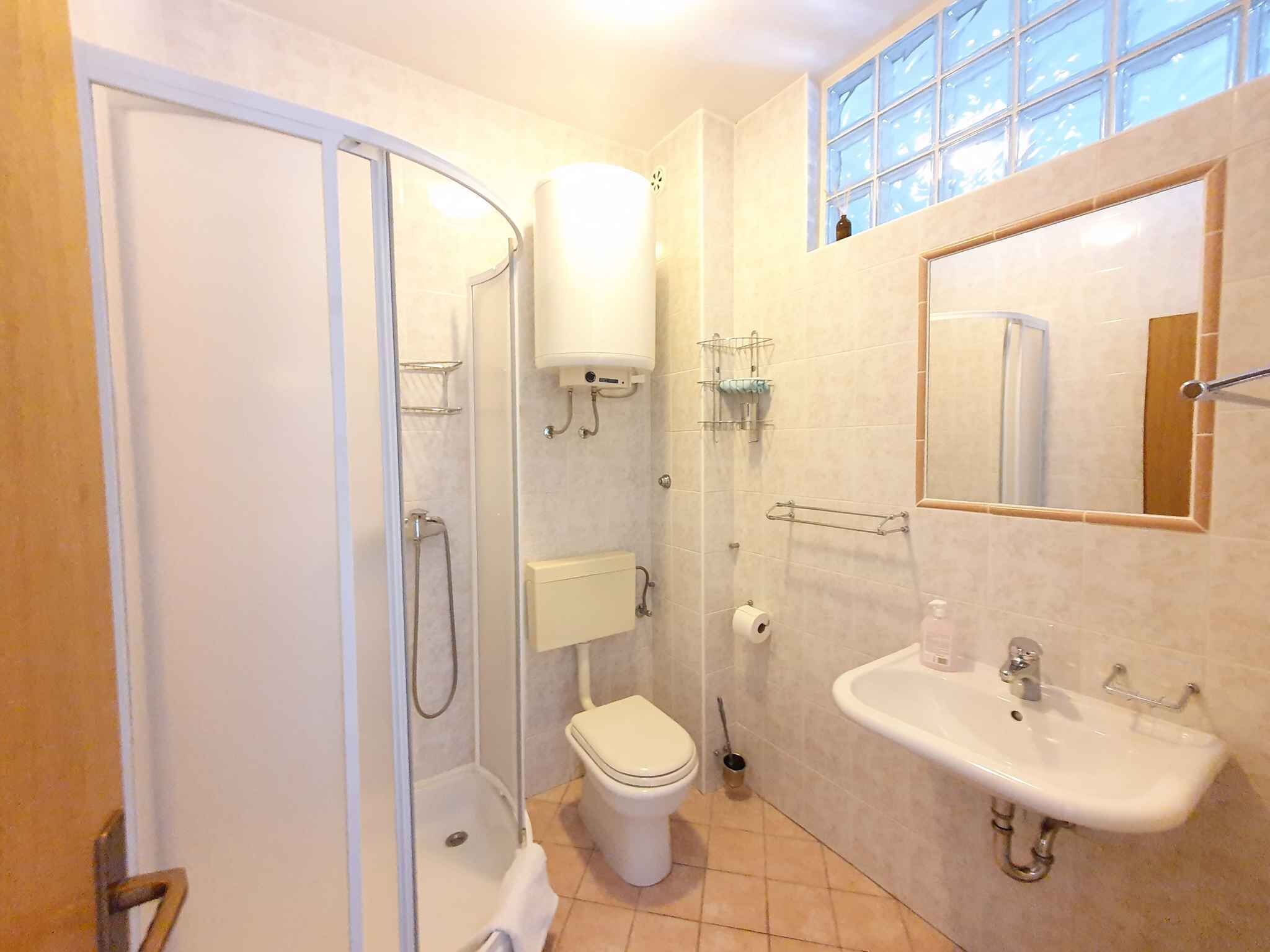 A bathroom with a shower, toilet, sink, and a window with a view.