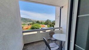 A balcony with a table and two chairs, a view of a hilly landscape, and a clear sky.
