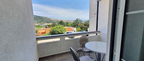 A balcony with a table and two chairs, a view of a hilly landscape, and a clear sky.