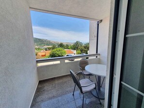 A balcony with a table and chairs, a view of a hilly landscape, and a building in the distance.