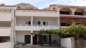 A two-story building with a balcony, a small garden area, and a stone wall.