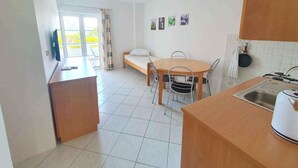 A compact kitchen with a dining table, chairs, a bed, and a TV.
