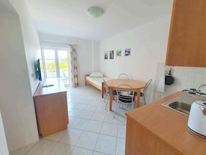 A compact kitchen with a dining table, chairs, a bed, and a TV.