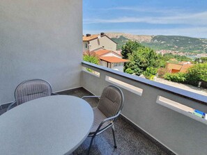 Un balcone con un tavolo rotondo e due sedie, affaccia su una città con case e colline.