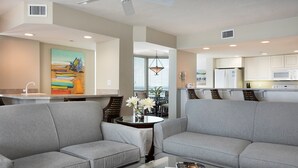 A modern living room with two grey sofas, a glass coffee table, and a painting on the wall. - Spacious Beachfront Suite | Access to Pool (Fort Myers Beach)