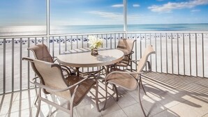 A balcony with a round table and wicker chairs, overlooking a beach with people and a clear sky. - Spacious Beachfront Suite | Access to Pool (Fort Myers Beach)