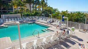 A poolside area with lounge chairs and a swimming pool, surrounded by palm trees and buildings. - Spacious Beachfront Suite | Access to Pool (Fort Myers Beach)