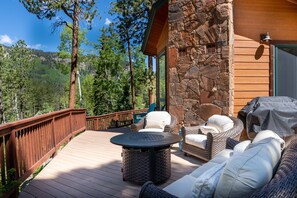 A wooden deck with wicker furniture, a stone wall, and a view of a forested area. - Hot Tub, Great Deck, Hiking/Fishing Close! (Durango)