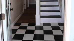 Ein Korridor mit einem schwarz-weiß kariertem Boden, einer weißen Treppe und einer Tür mit Fenster.