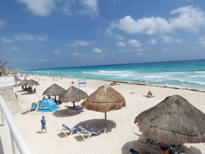 A beach with thatched umbrellas, lounge chairs, and a clear view of the ocean. - Wake up in Caribbean Paradise 1304 (Cancún)