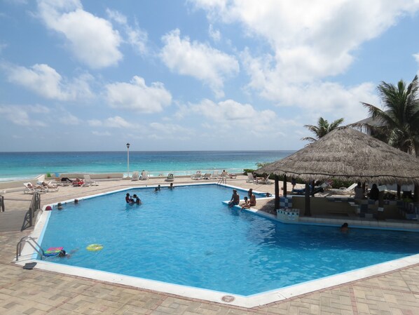A swimming pool with a thatched-roof structure, lounge chairs, and a view of the ocean. - Wake up in Caribbean Paradise 1304 (Cancún)