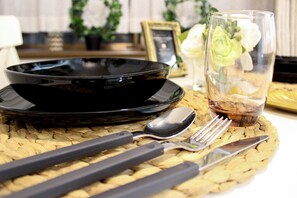 Une table dressée avec une assiette noire, une cuillère, une fourchette et un verre contenant une boisson, le tout posé sur un set de table en fibres tressées.