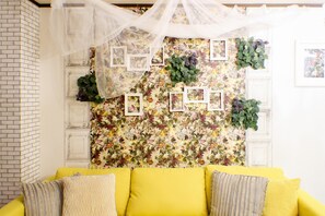 Une pièce avec un canapé jaune, un papier peint à motifs floraux et des tableaux encadrés.