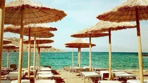 A beach with rows of sun umbrellas and lounge chairs facing the sea. - Daskalio Resort Adamis (Lavreotiki)