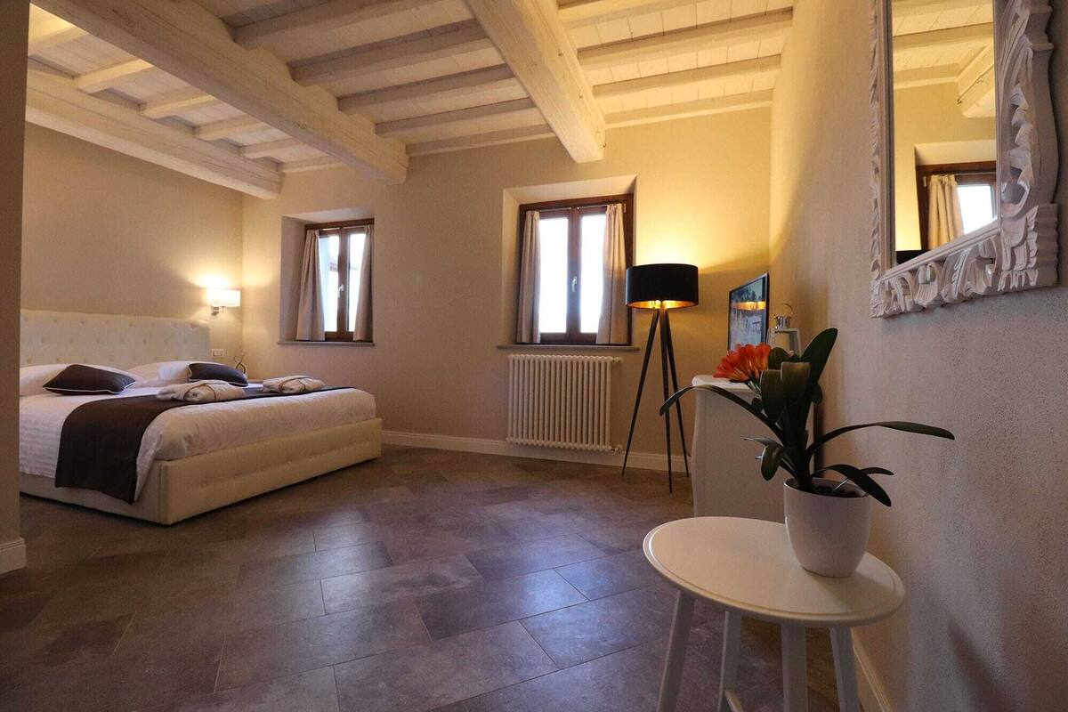 Een slaapkamer met een bed, bedlampjes, een radiator, een kamerplant en een spiegel aan de muur.