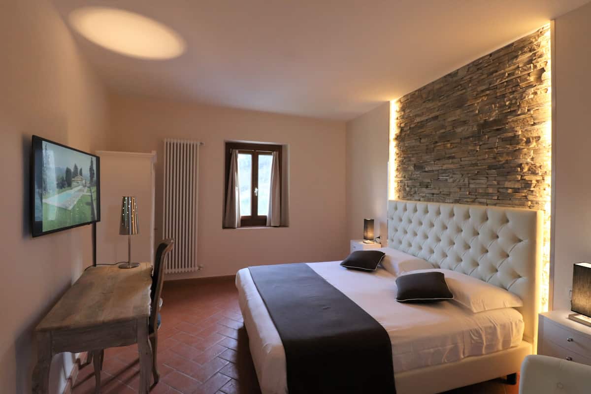 Een slaapkamer met een groot bed, een accentmuur van steen, een bureau en een radiator.
