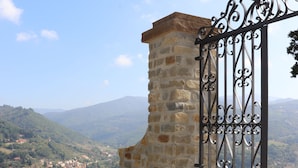 A stone wall with a metal gate, overlooking a town with mountains in the background. - Il Borgo di Villa Cellaia (Dicomano)