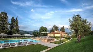 A pool area with lounge chairs and umbrellas, a stone patio, and a house with a tiled roof. - Il Borgo di Villa Cellaia (Dicomano)
