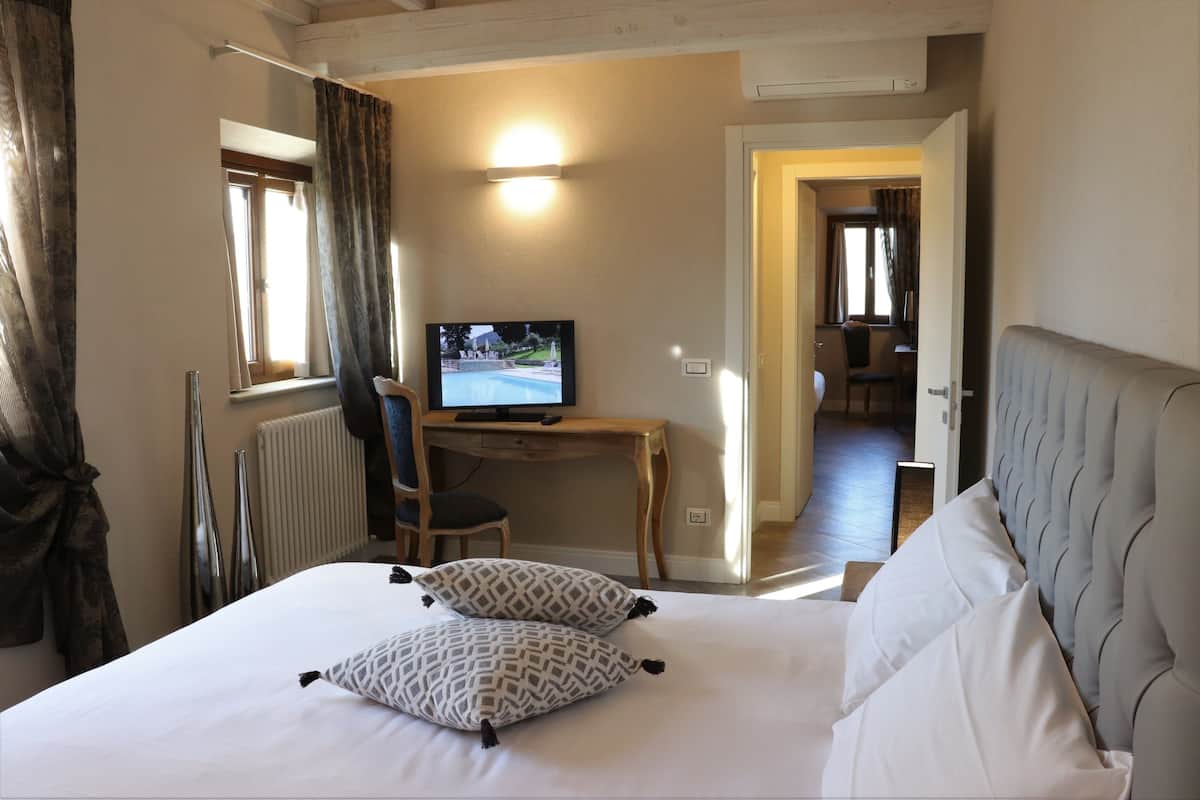Een hotelkamer met een bed, een bureau met een computer, een televisie en uitzicht op de gang.