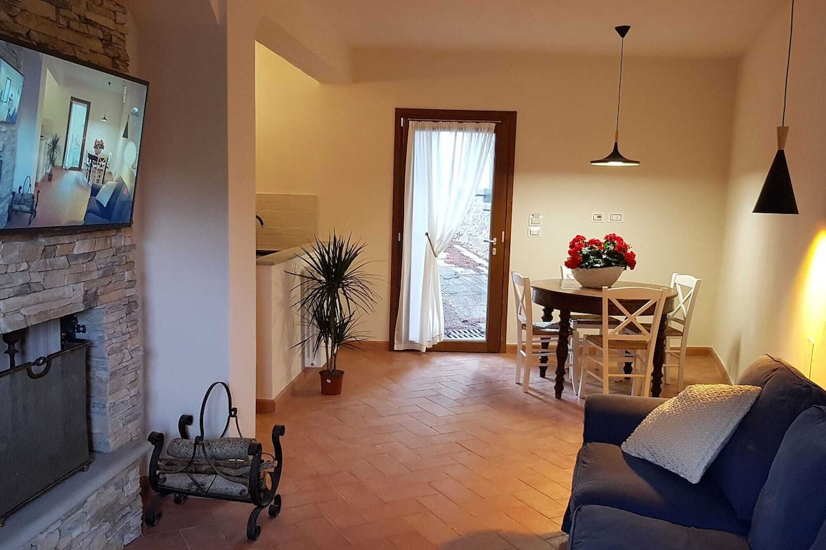 Een woonkamer met een open haard, een eetgedeelte met een tafel en stoelen, en een moderne hanglamp.
