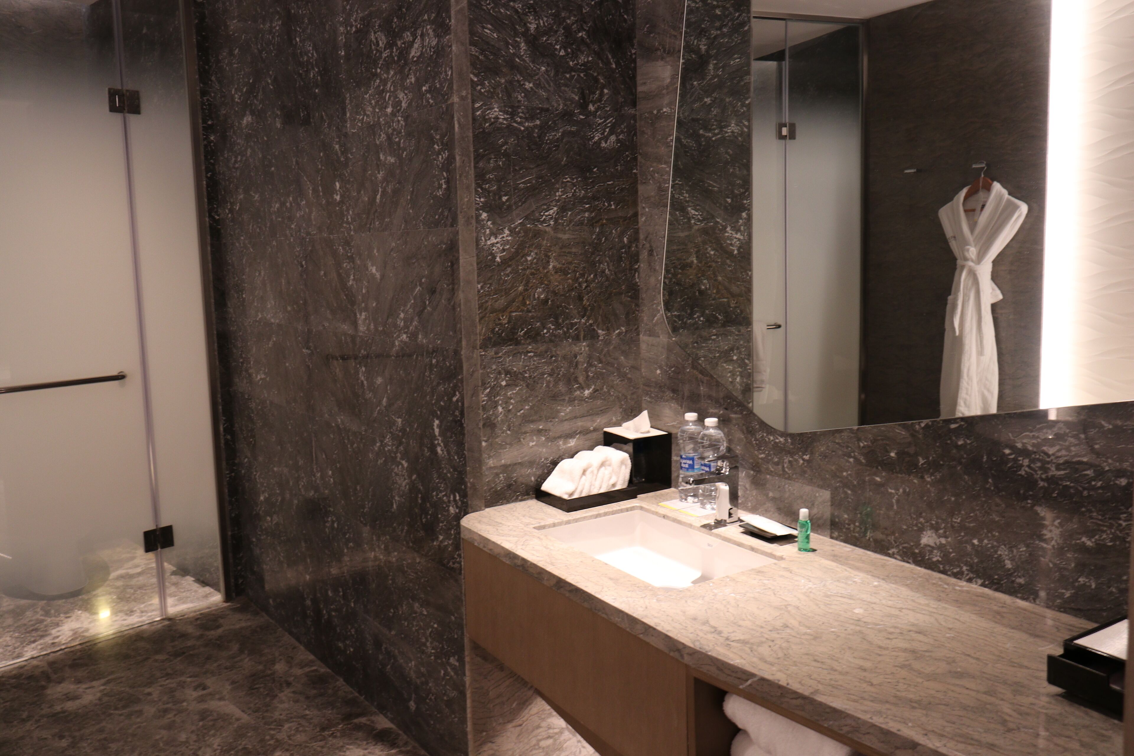 A modern bathroom with a marble sink, a glass shower enclosure, and a robe hanging on the wall.