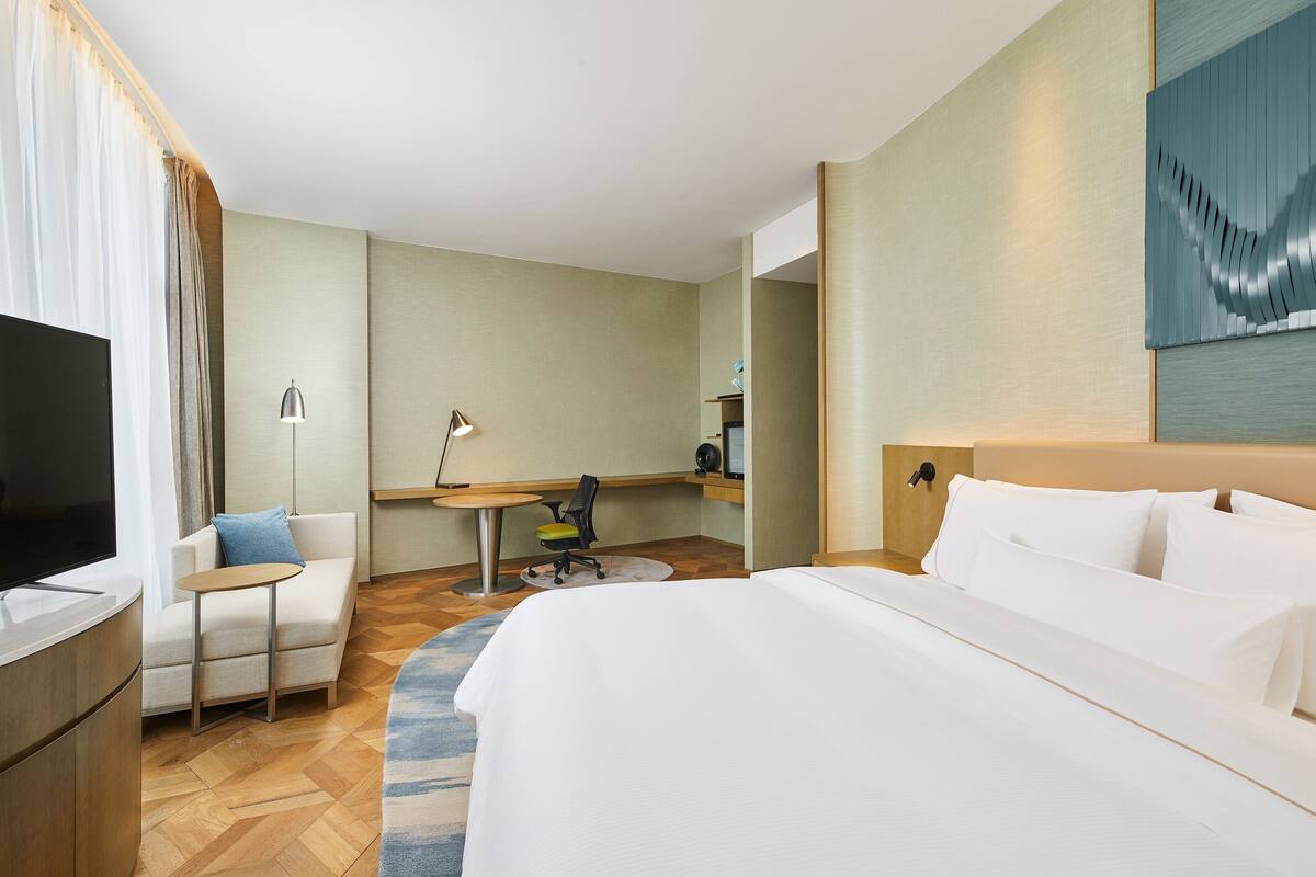 A hotel room with a large bed, a desk with a chair, a television, and a lamp.