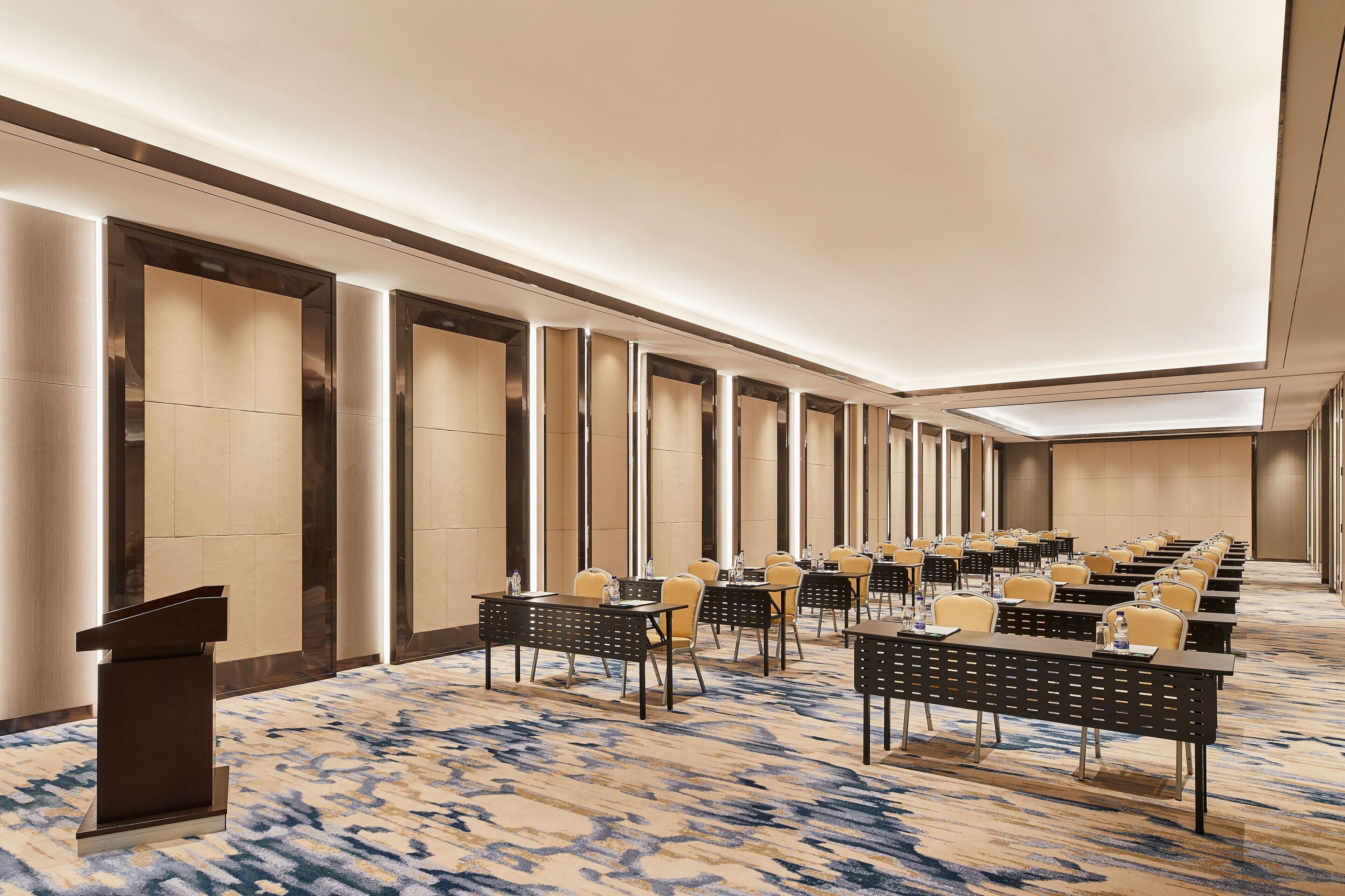 A conference room with rows of tables and chairs, a podium, and a patterned carpet.