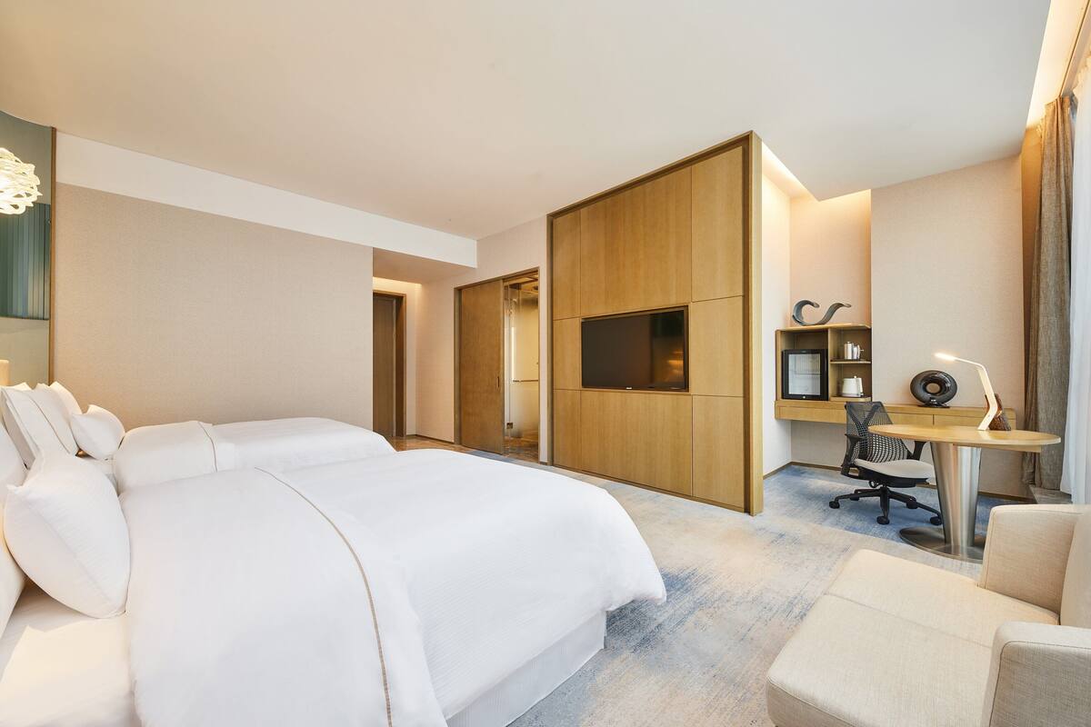 A hotel room with a large bed, a desk with a chair, a TV, and a wardrobe.