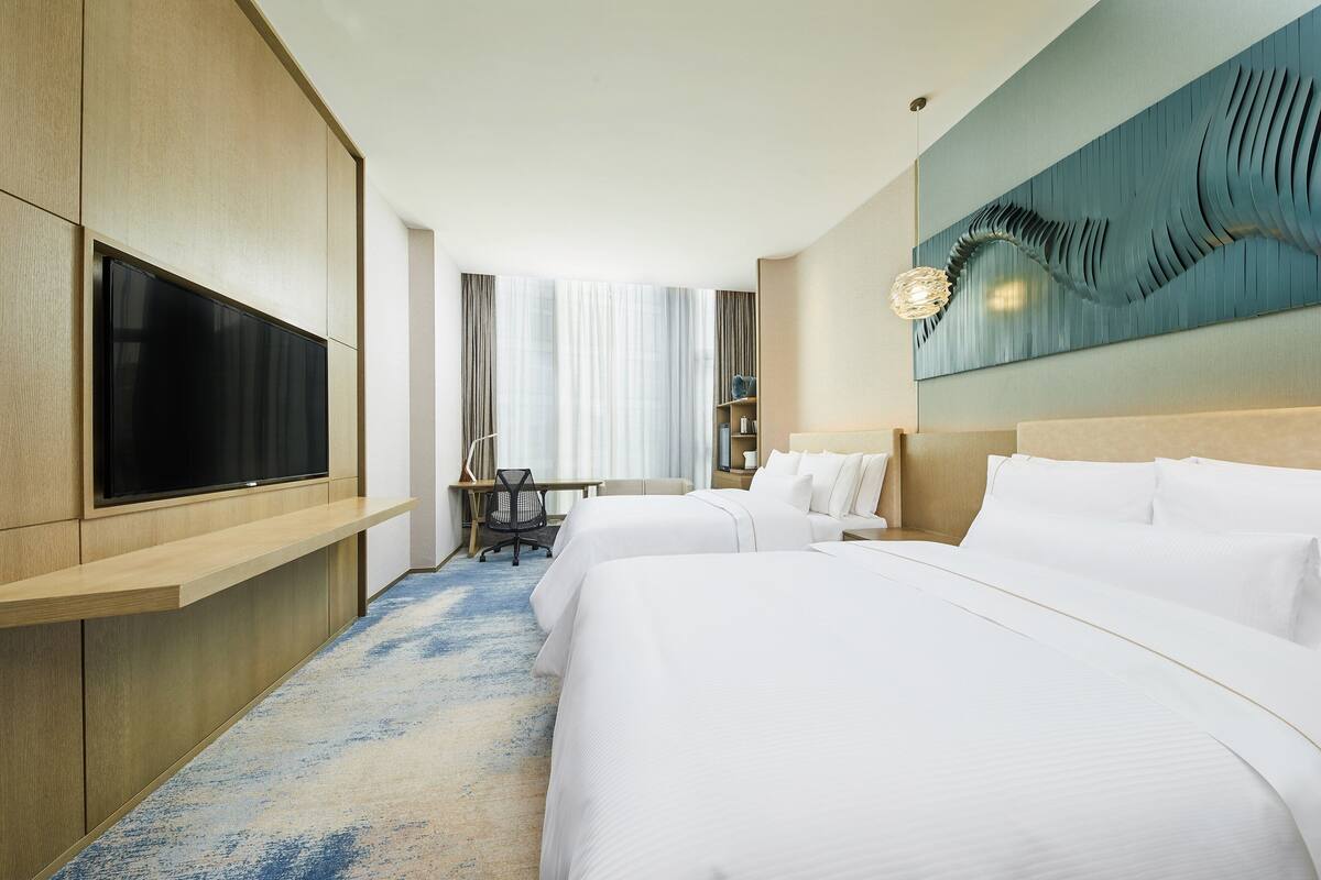 A hotel room with two beds, a flat-screen TV, a desk, and a large abstract painting on the wall.