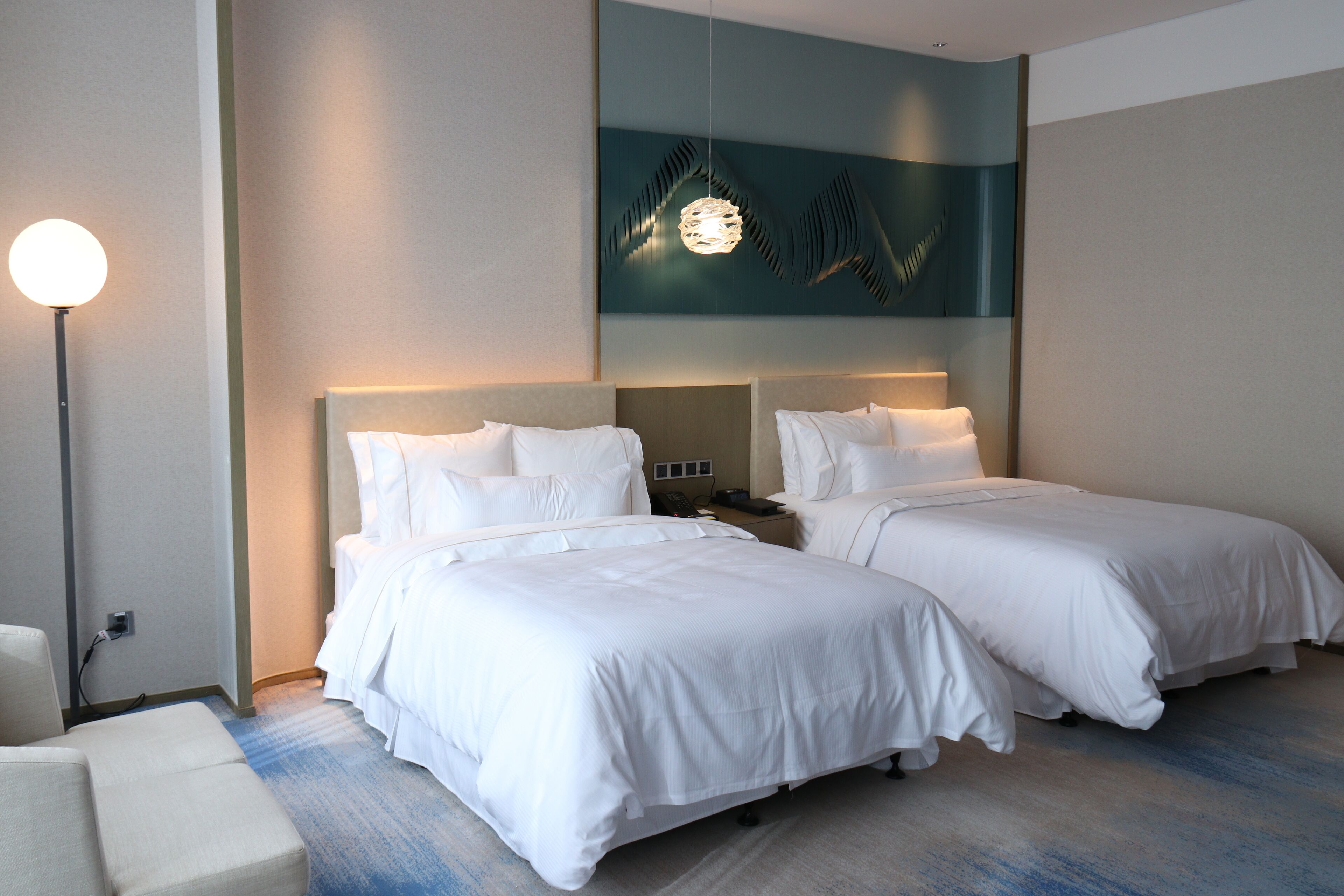 A hotel room with two beds, a nightstand, a lamp, and a wall art piece.