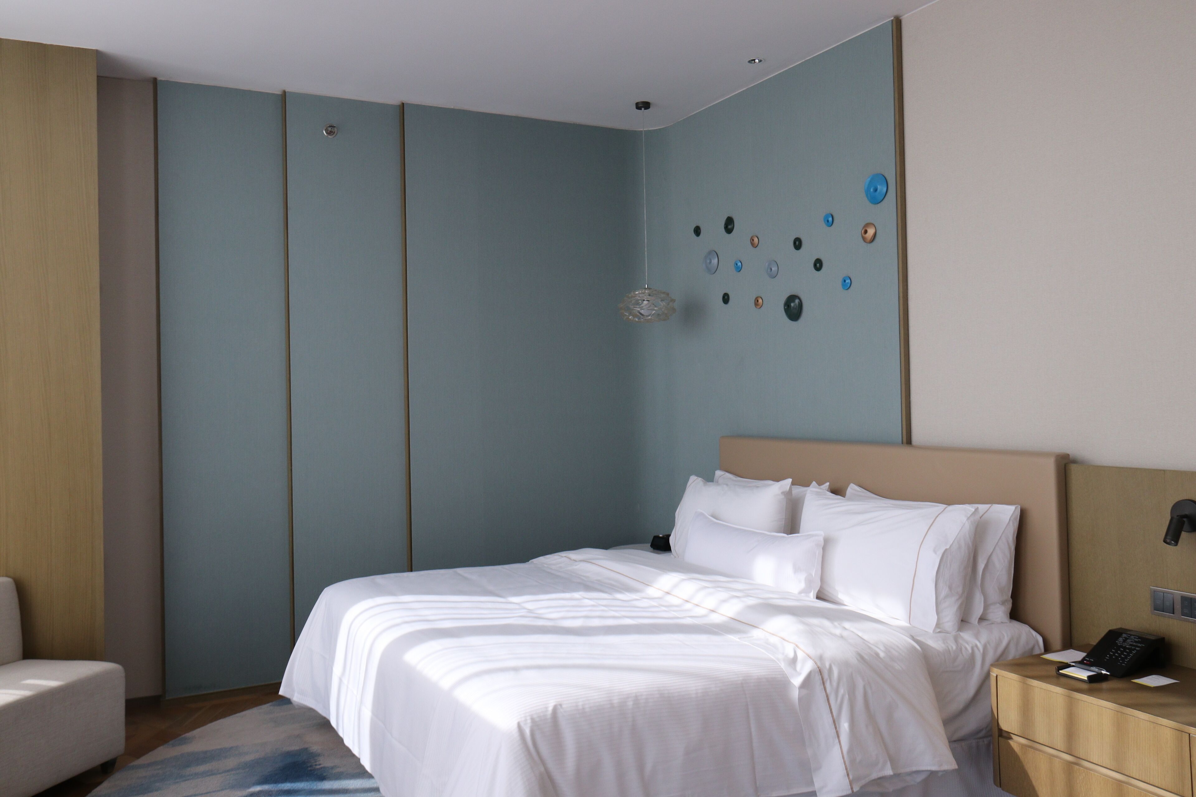 A hotel room with a bed, bedside table, and a wall with decorative buttons.