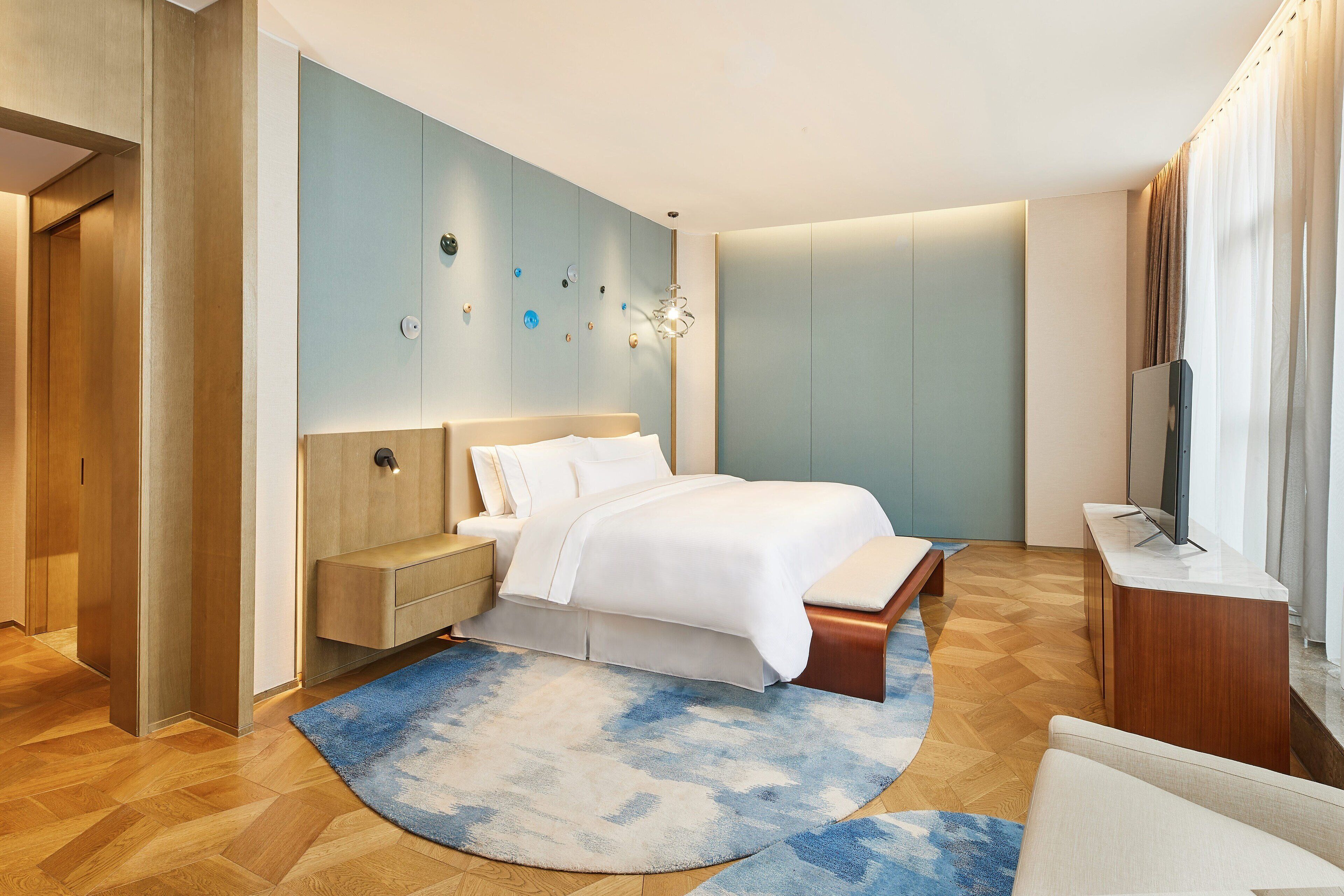 A modern bedroom with a large bed, bedside tables, a TV, and a wooden floor.