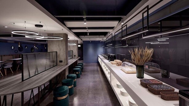A modern, minimalist restaurant interior with a long counter, round stools, and a central decorative vase. - Haifu Hotel & Suites (Jincheng)