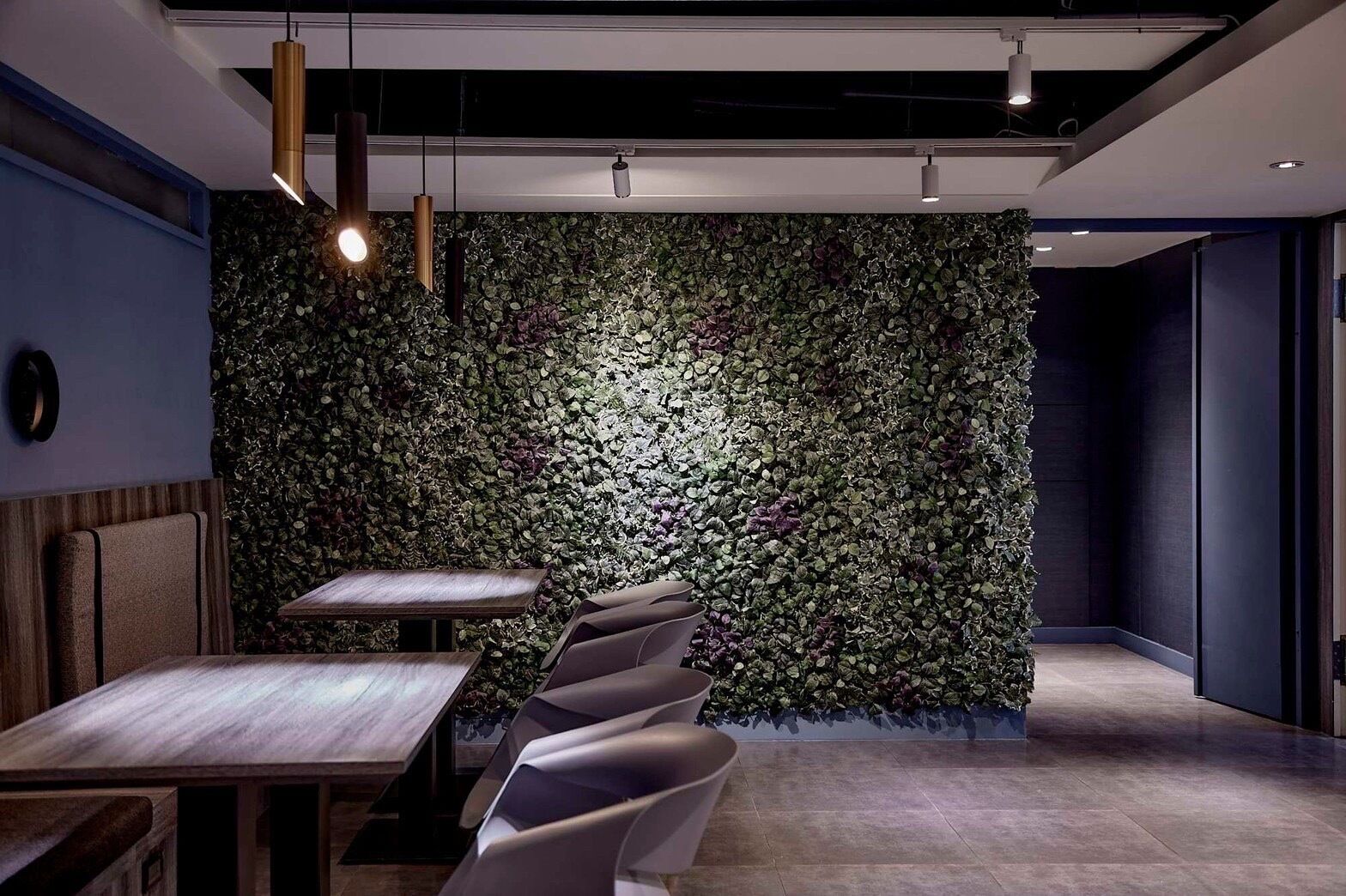 A modern conference room with a green leafy wall, a wooden table, and grey chairs.