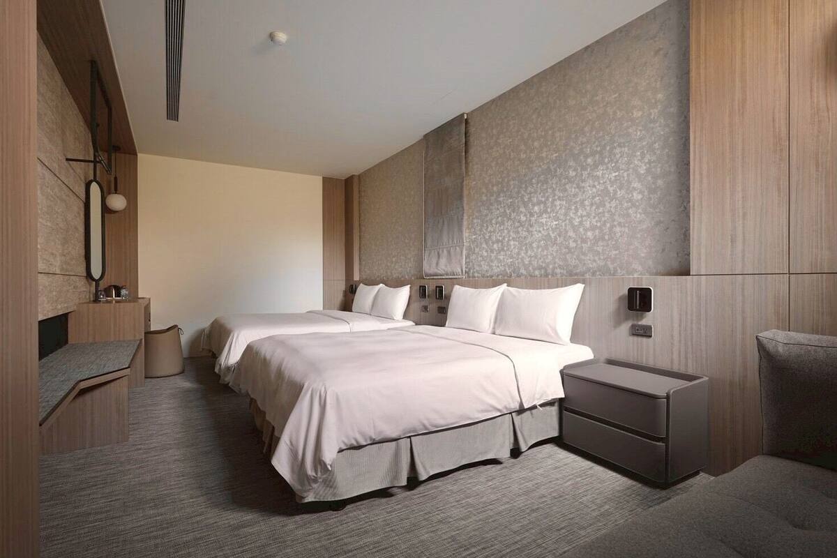 Une chambre d’hôtel moderne avec deux lits, une table de chevet, une chaise et un grand miroir.
